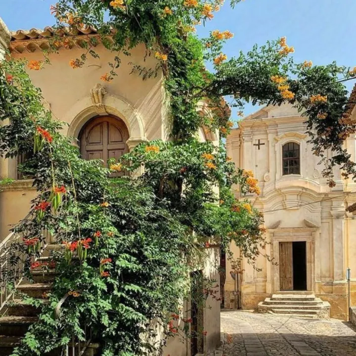 Quiet Sicilian square with flowering plants and a church facade